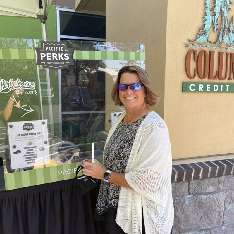 A woman smiling with her ice cream sundae by an outdoor Pacific Perks mobile café at a Columbia Credit Union event