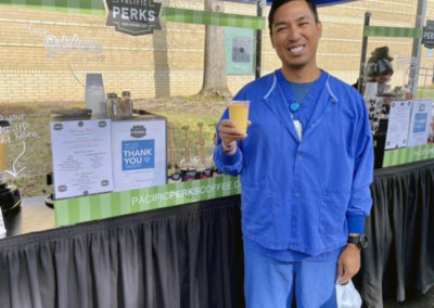 a person smiling while holding a smoothie next to a Pacific Perks mobile café at a Kaiser Cascade Park event