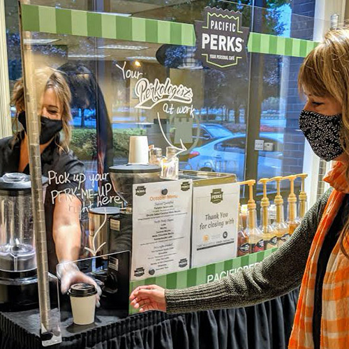 a Perkologist serves a coffee drink through a plexiglass window at a COVID-safe Pacific Perks espresso mobile café