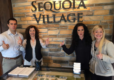 a group posing with thumbs up in front of a Sequoia Village sign