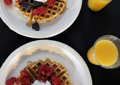 an overhead view of two plates of Pacific Perks waffles with berries and cream with cups of orange juice during a Bridgetown resident event