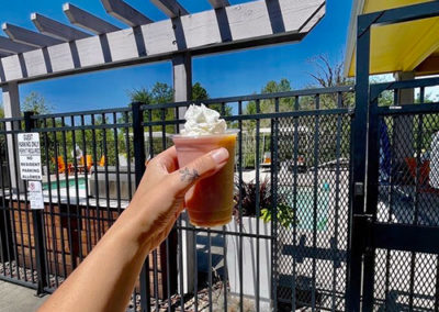 a hand holding a Pacific Perks smoothie by an outdoor pool