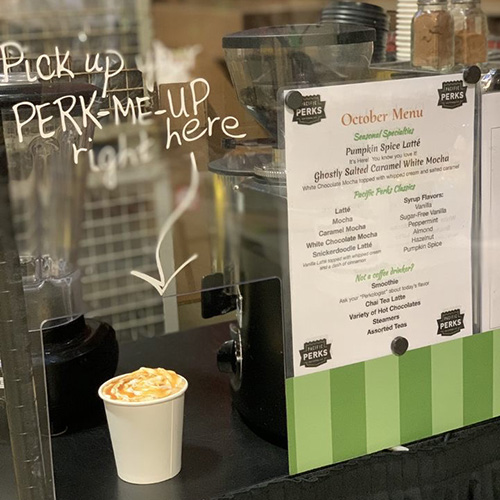 an coffee drink sitting at a Pacific Perks espresso mobile café with "pick up perk-me-up right here" written on the plexiglass above it