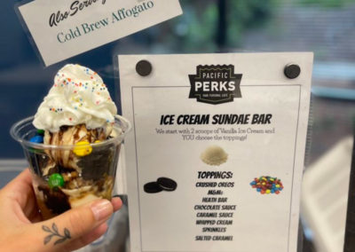 a hand holding a Pacific Perks ice cream sundae up to the menu listing all of the available toppings