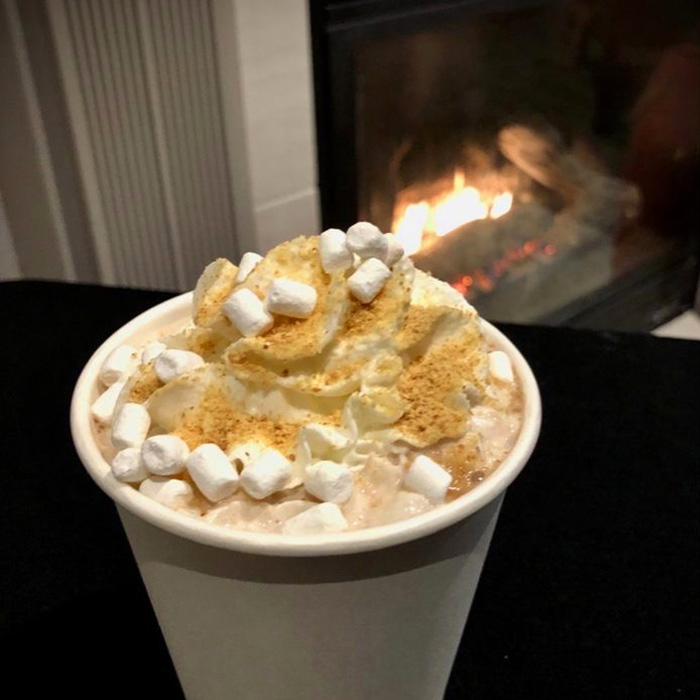 a Pacific Perks hot cocoa with s'more toppings in front of a fireplace