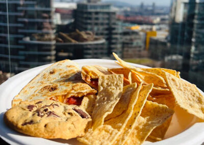 a plate of Pacific Perks quesadilla with chips and cookie, downtown city buildings in the background
