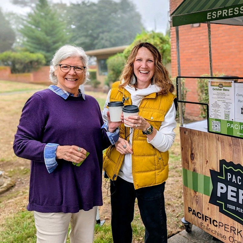 two people smiling holding their drinks at an outdoors event with a Pacific Perks espresso bar mobile café