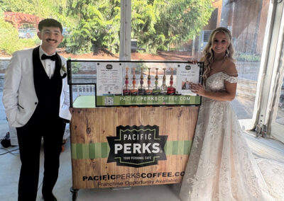 bride and groom standing and smiling next to a Pacific Perks cart at their wedding